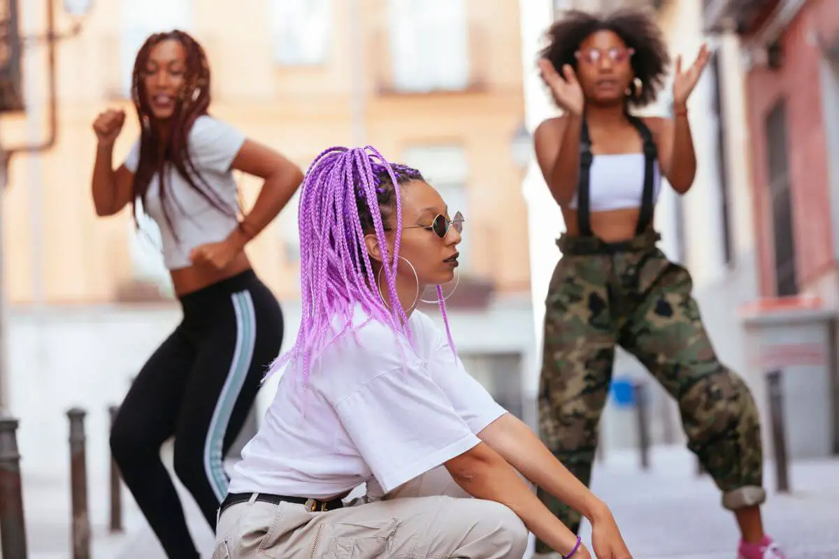 Three Black women dancing outside on the street.