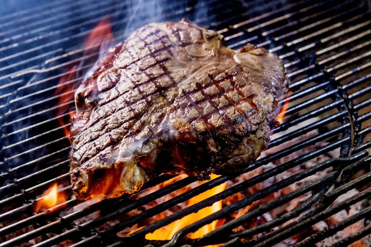 A seared porterhouse being grilled on a charcoal grill.